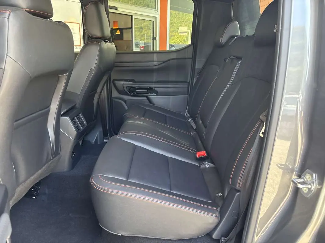 Vue intérieure côté droit des sièges arrière en cuir noir avec surpiqûres orange du Ford Ranger Wildtrak Plus gris carbone 2026.