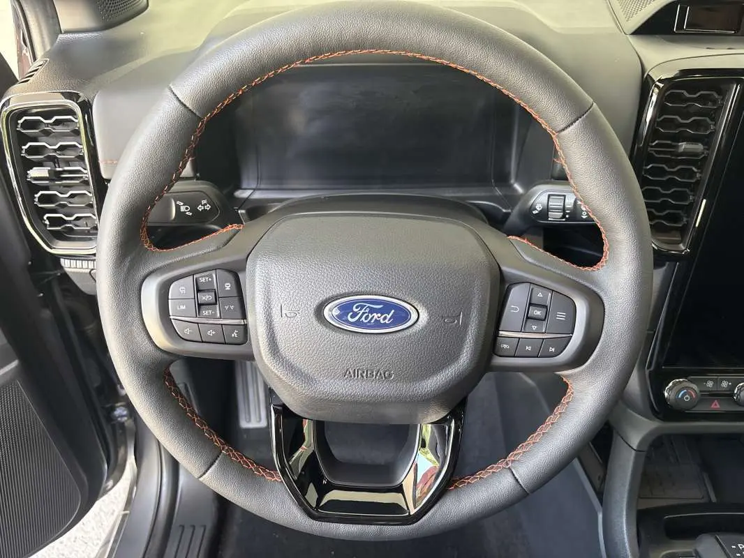 Vue rapprochée du volant cuir noir avec surpiqûres orange du Ford Ranger Wildtrak Plus 2026, tableau de bord partiel visible.