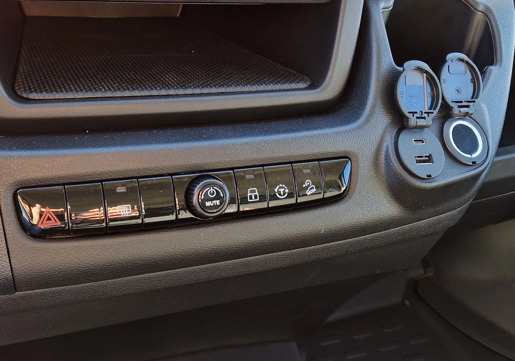 Détail de la console centrale noire du Fiat Ducato Chassis Benne 2023 avec boutons de contrôle et prises USB ouvertes.
