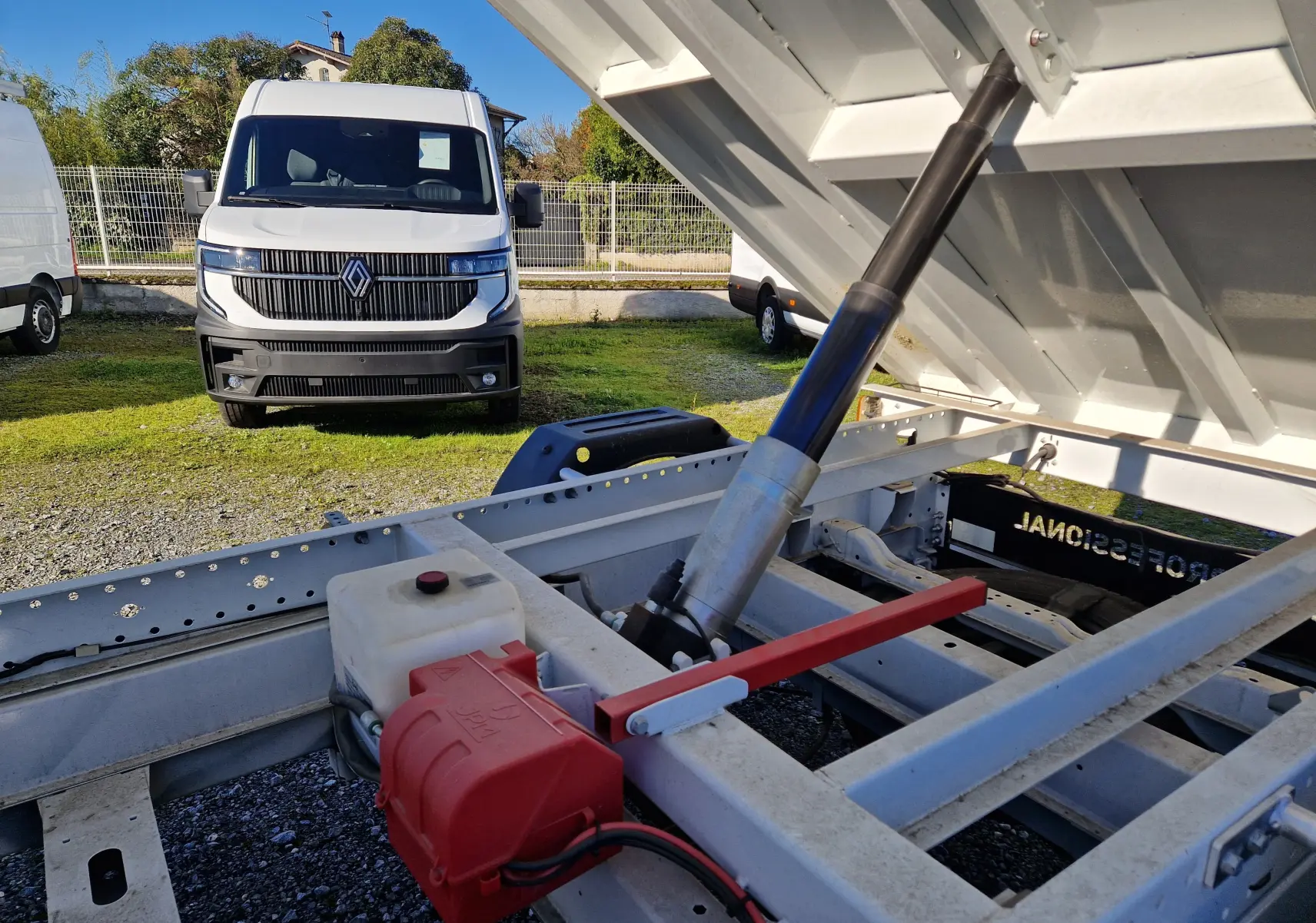 Vue rapprochée du mécanisme de benne relevée d’un FIAT Ducato blanc, avec un fourgon blanc en arrière-plan.