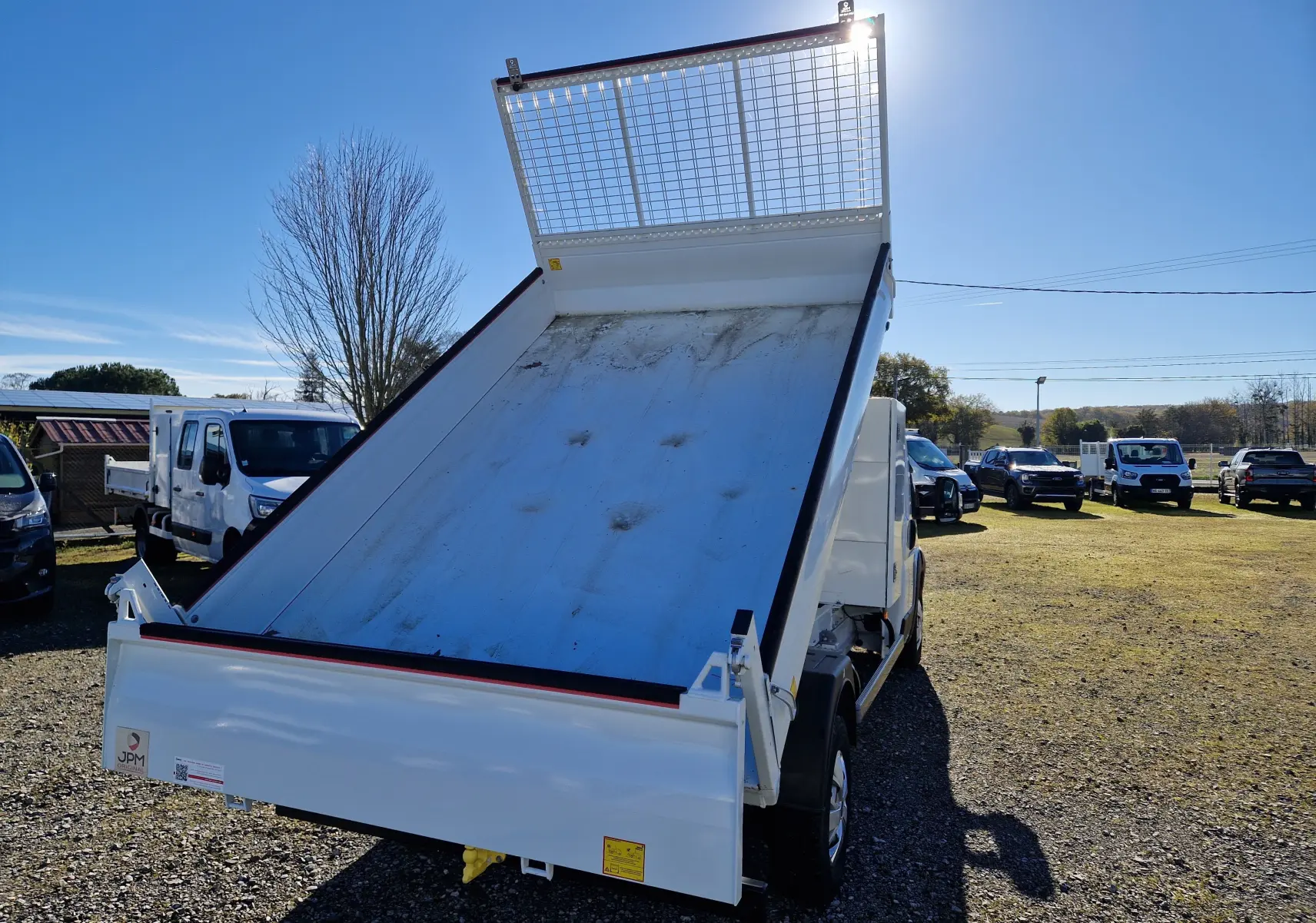 Vue arrière d'un FIAT Ducato Chassis Benne blanc 2023 avec benne acier JPM relevée sous un ciel bleu.