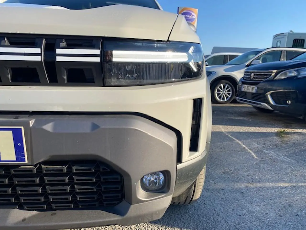 Gros plan sur l'avant droit du Dacia Duster beige Sandstone 2025, mettant en valeur ses phares LED et sa calandre noire.