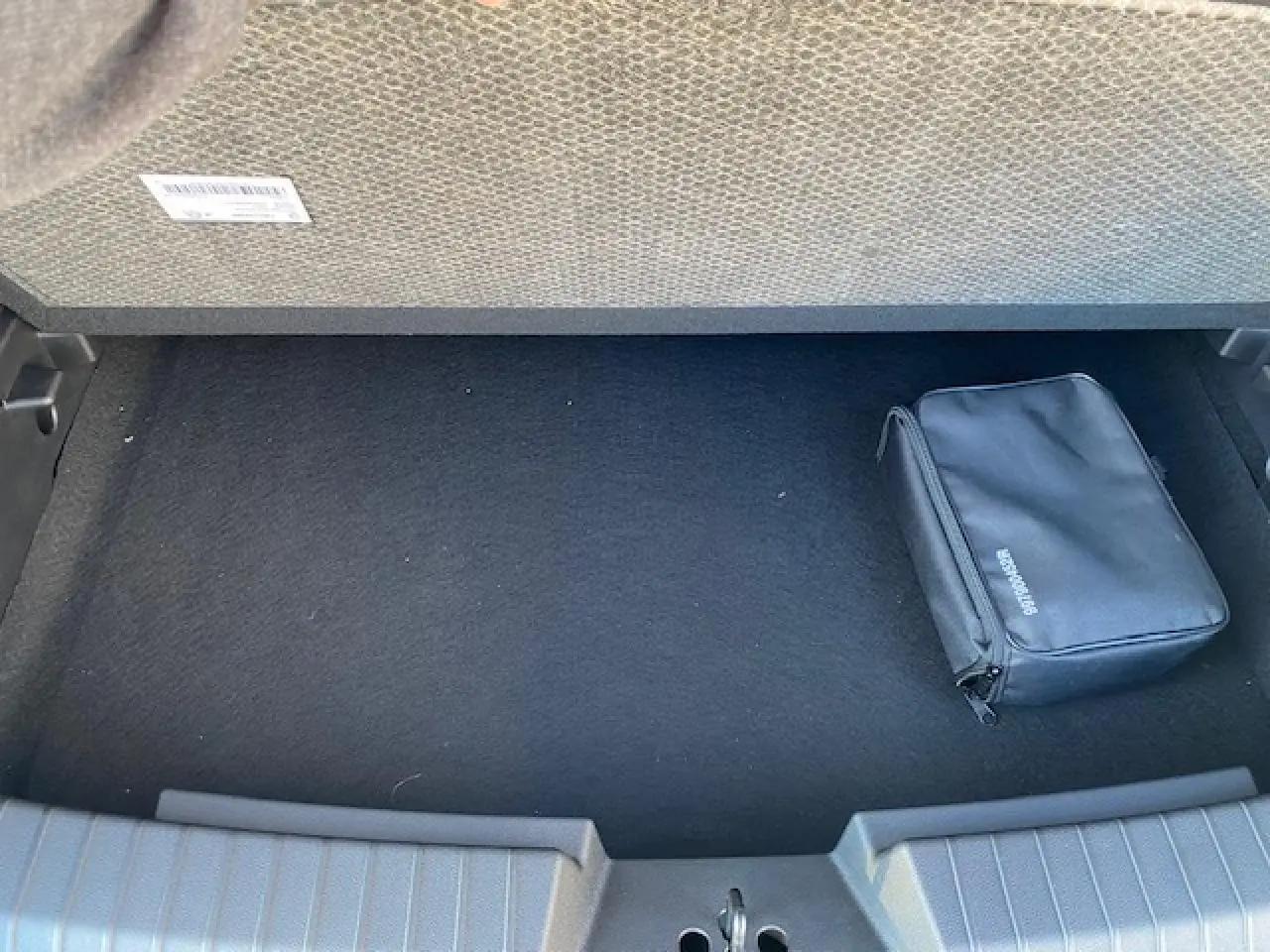 Coffre ouvert d'un Dacia Duster 2025 beige Sandstone, vue intérieure avec un sac noir de secours posé à droite.