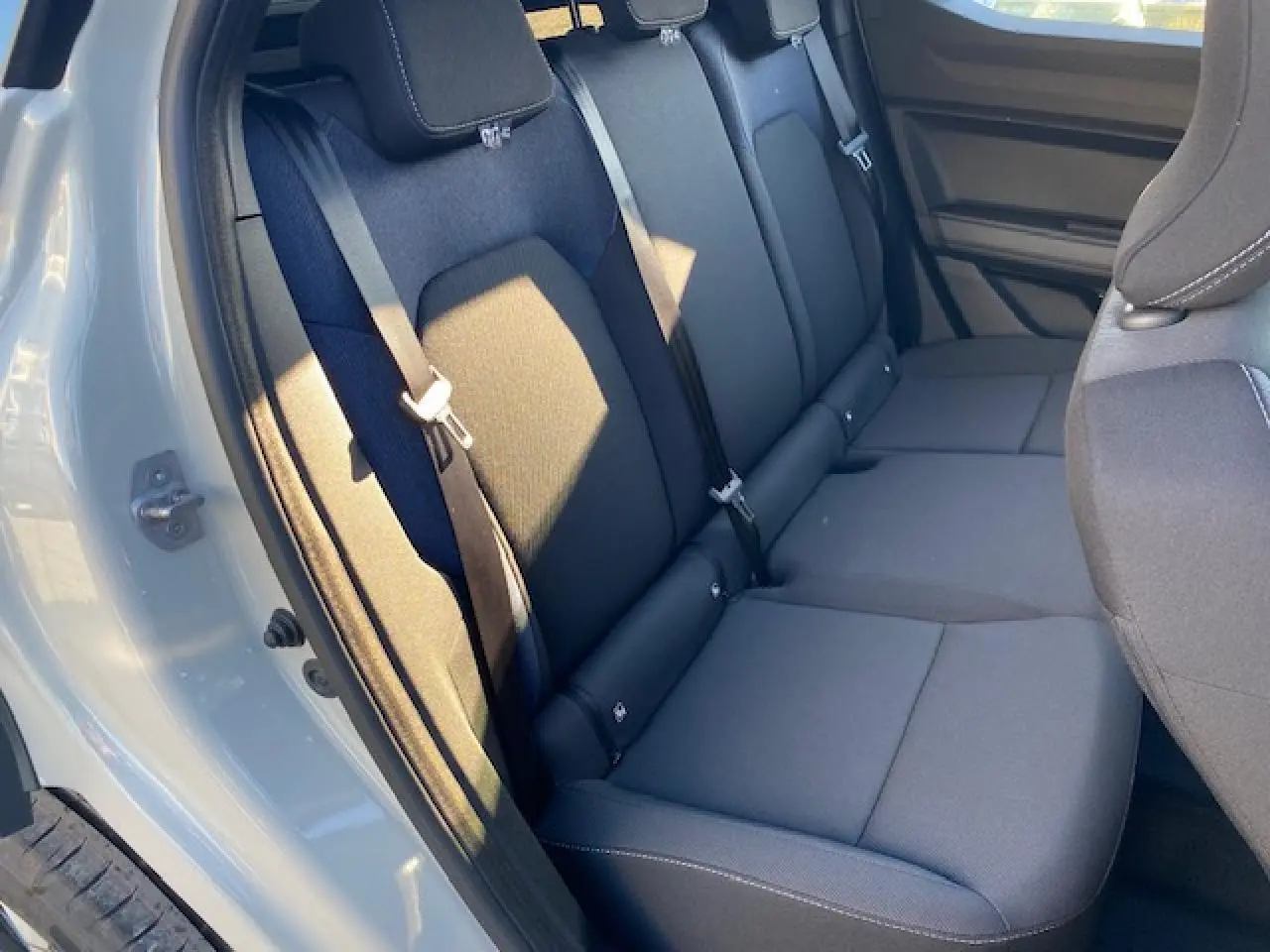 Vue intérieure sur les sièges arrière noirs du Dacia Duster 2025, porte arrière beige sandstone ouverte côté gauche.