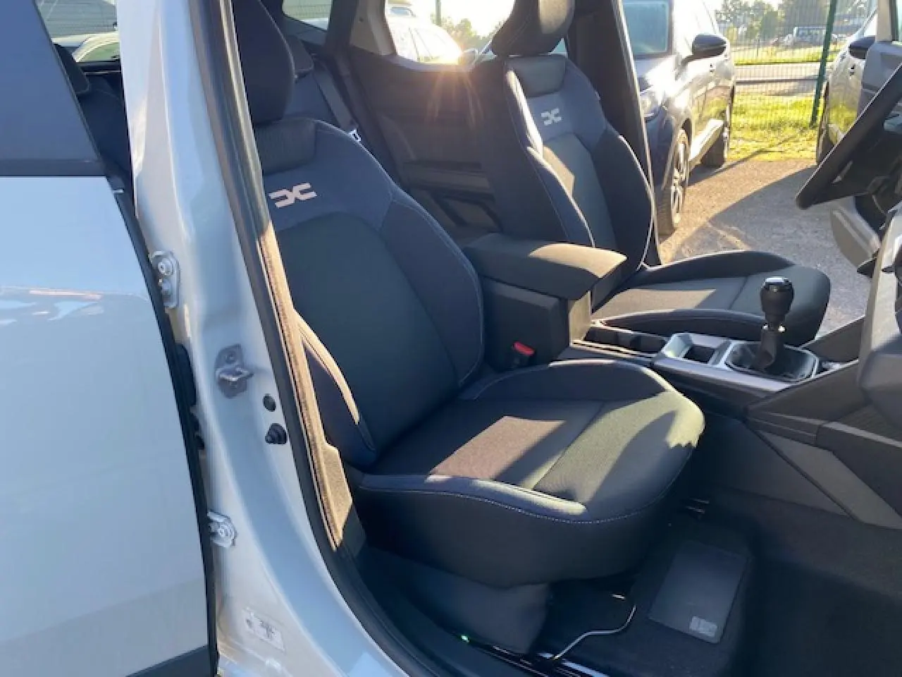 Vue intérieure côté conducteur du Dacia Duster 2025 avec sièges noirs et levier de vitesse manuel visible.