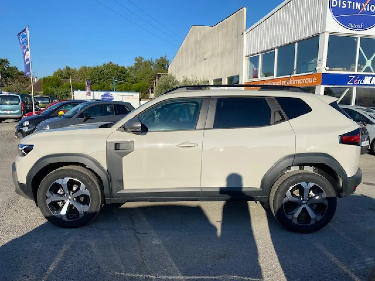Profil côté gauche du SUV Dacia Duster 2025 beige Sandstone avec jantes noires et détails noirs contrastants.