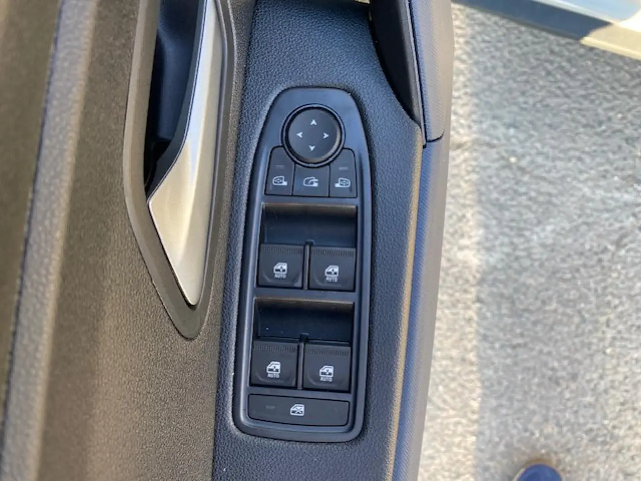 Gros plan sur les commandes des vitres électriques et rétroviseurs sur la portière côté gauche d'un Dacia Duster beige Sandstone 2025.