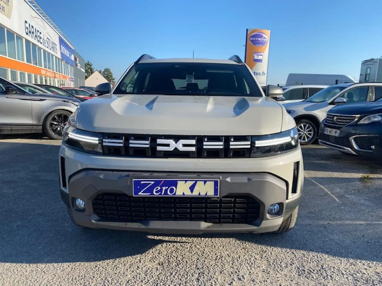 Vue frontale du Dacia Duster 2025 beige Sandstone avec calandre noire et plaque d'immatriculation Zero KM visible.