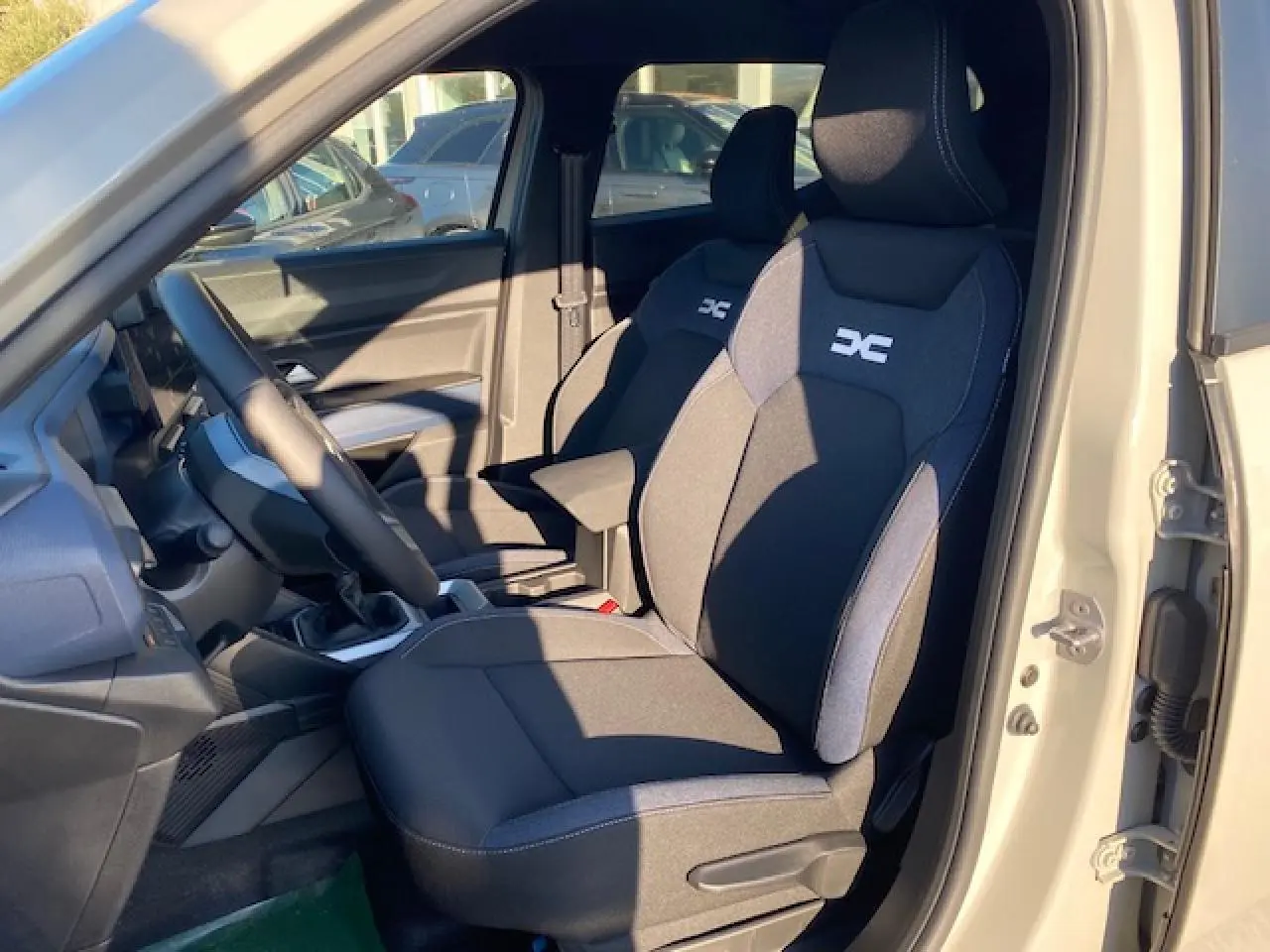 Intérieur du Dacia Duster 2025 beige Sandstone, vue côté conducteur sur les sièges sport noirs avec logo DC brodé.