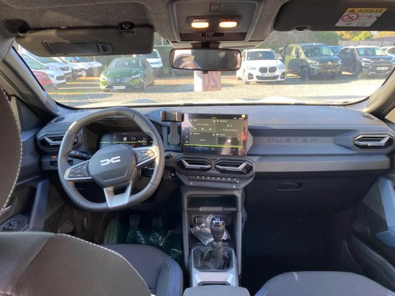 Vue intérieure avant du Dacia Duster 2025 beige sandstone, avec tableau de bord moderne et boîte manuelle visible.