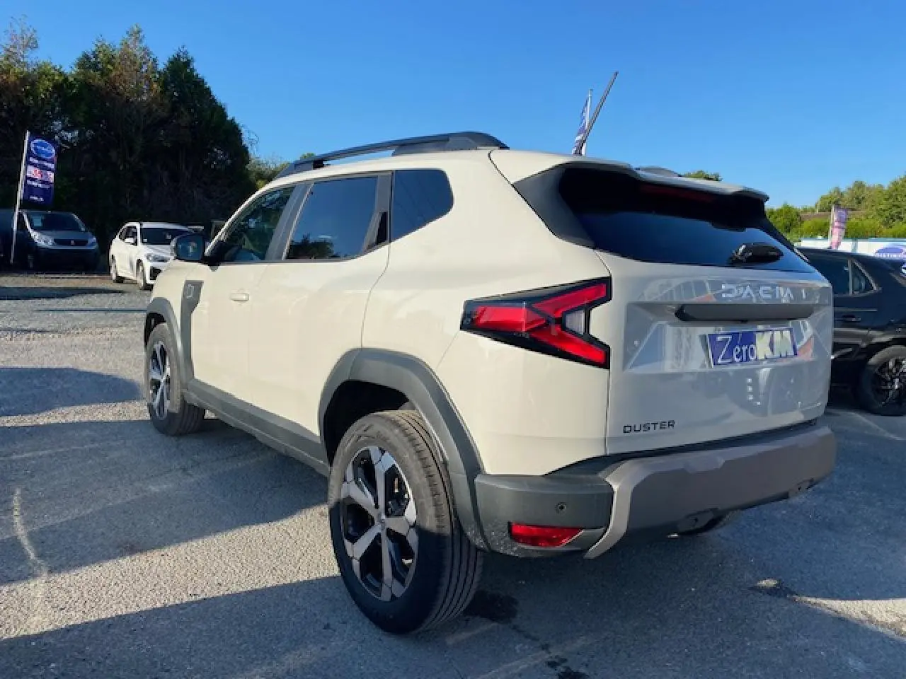 Dacia Duster 2025 beige Sandstone vu en 3/4 arrière droit, avec feux arrière en forme de flèche et jantes noires.