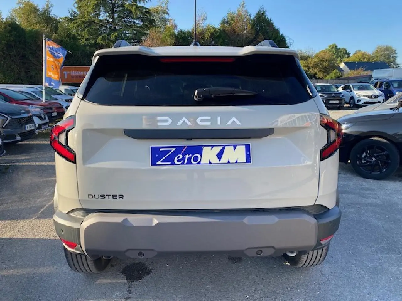 Vue arrière du Dacia Duster 2025 beige Sandstone avec feux arrière en forme de C et plaque Zéro KM visible.