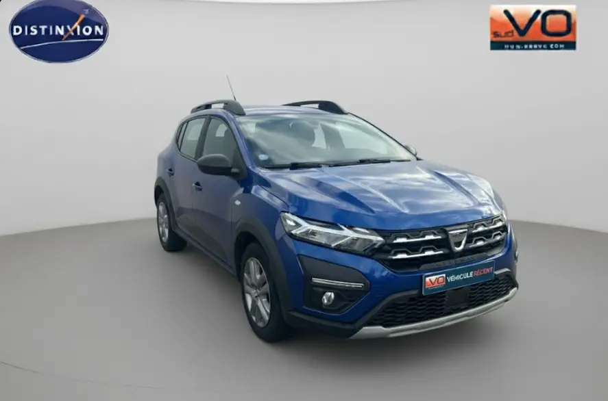 Dacia Sandero Stepway bleu foncé vue 3/4 avant droit avec barres de toit et feux allumés sur fond neutre.