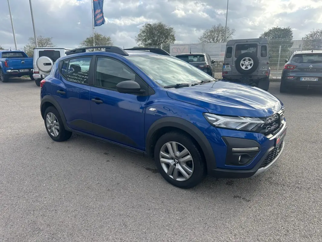 Dacia Sandero Stepway bleu foncé vue 3/4 avant droit avec barres de toit et vitres surteintées.