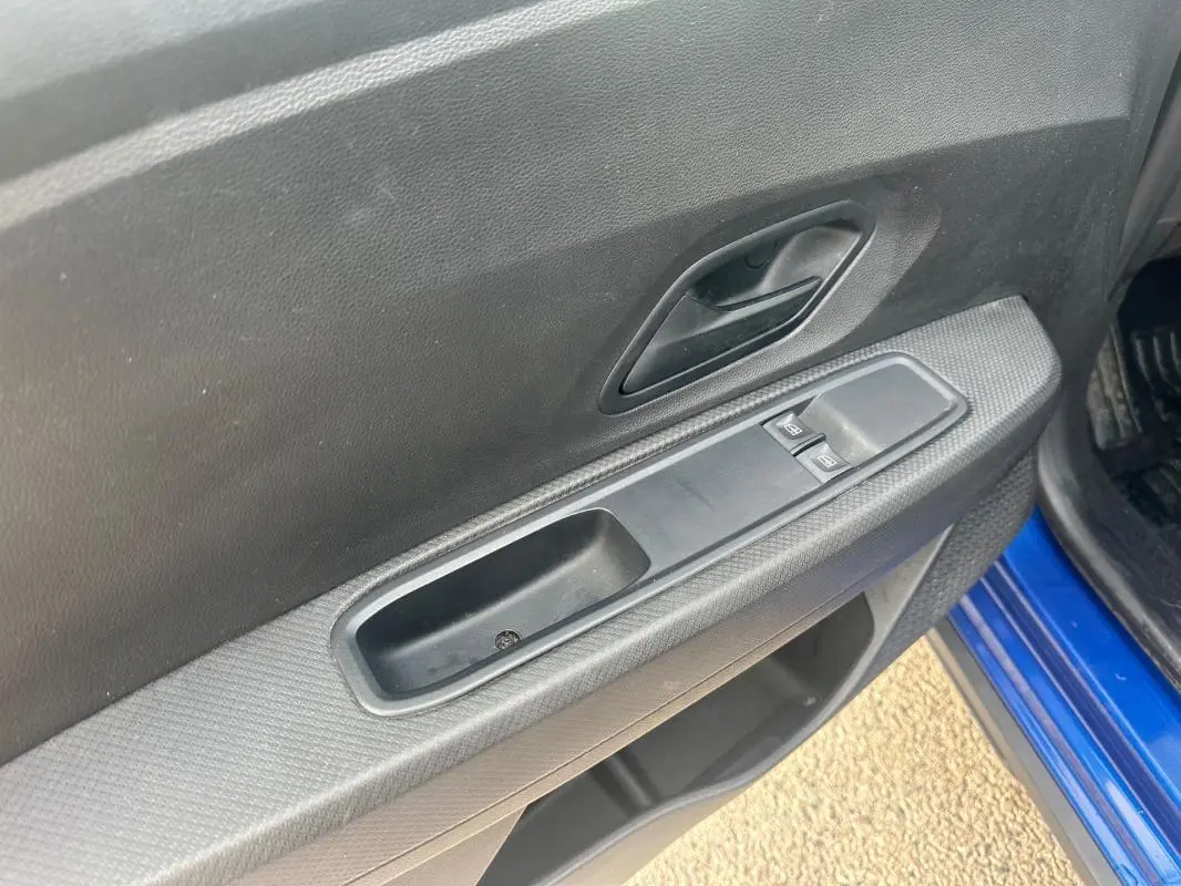 Gros plan sur la porte avant gauche bleu foncé d'une Dacia Sandero Stepway avec commandes des vitres électriques.