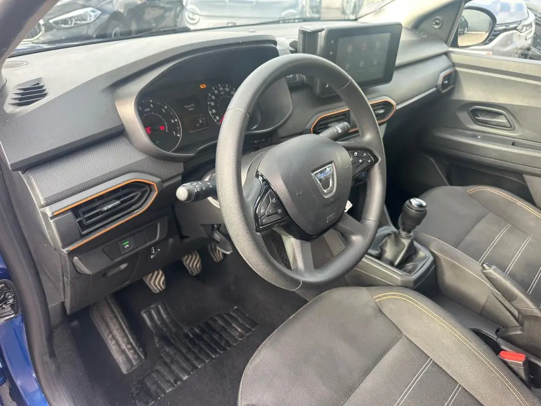 Intérieur de la Dacia Sandero bleu foncé 2021, vue côté conducteur avec volant, tableau de bord et boîte manuelle visibles.