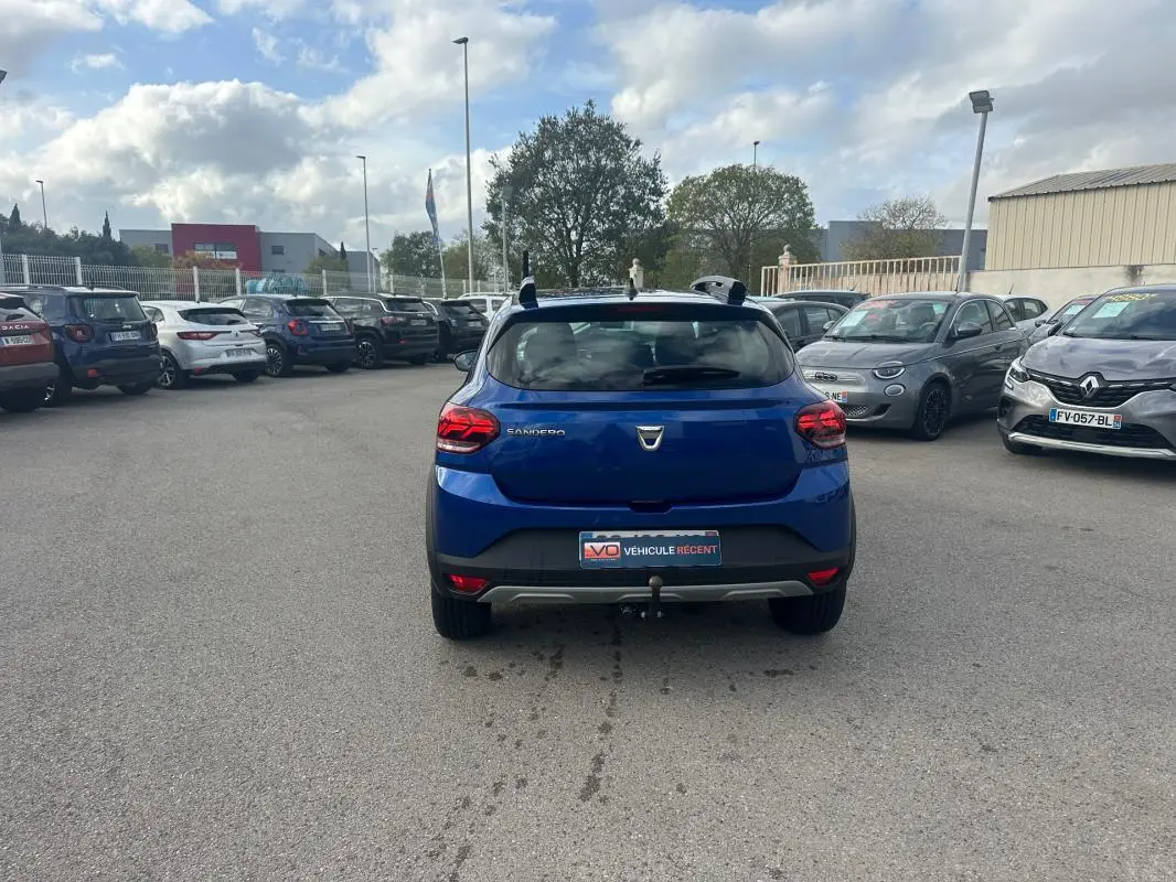 Vue arrière d'une Dacia Sandero Stepway bleu foncé avec barres de toit et attelage sur un parking.