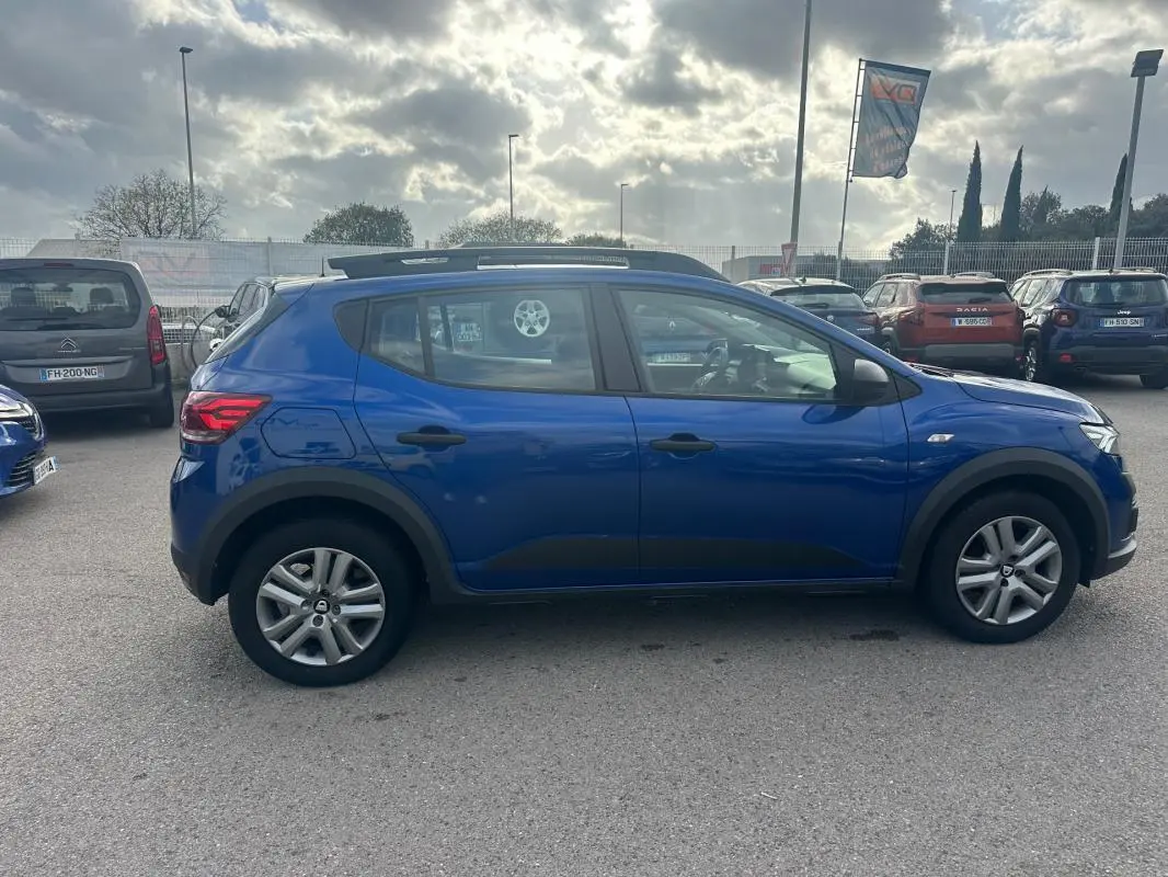 Vue latérale droite d'une Dacia Sandero Stepway bleu foncé avec barres de toit et vitres surteintées.