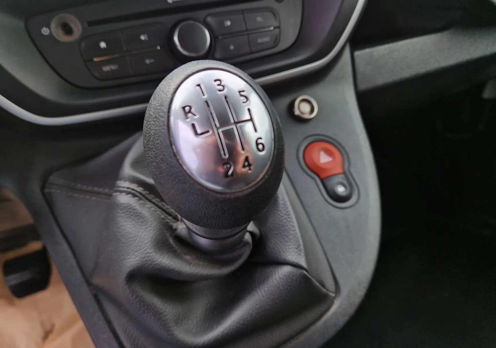 Gros plan sur le levier de vitesses manuel du Renault Kangoo 2020, entouré de commandes et d'un bouton d'alerte rouge.