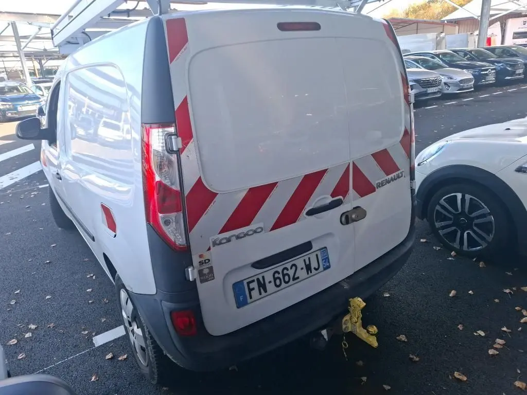 Vue 3/4 arrière droite d’un Renault Kangoo blanc avec bandes rouges réfléchissantes sur les portes arrière, stationné sur un sol gravillonné.