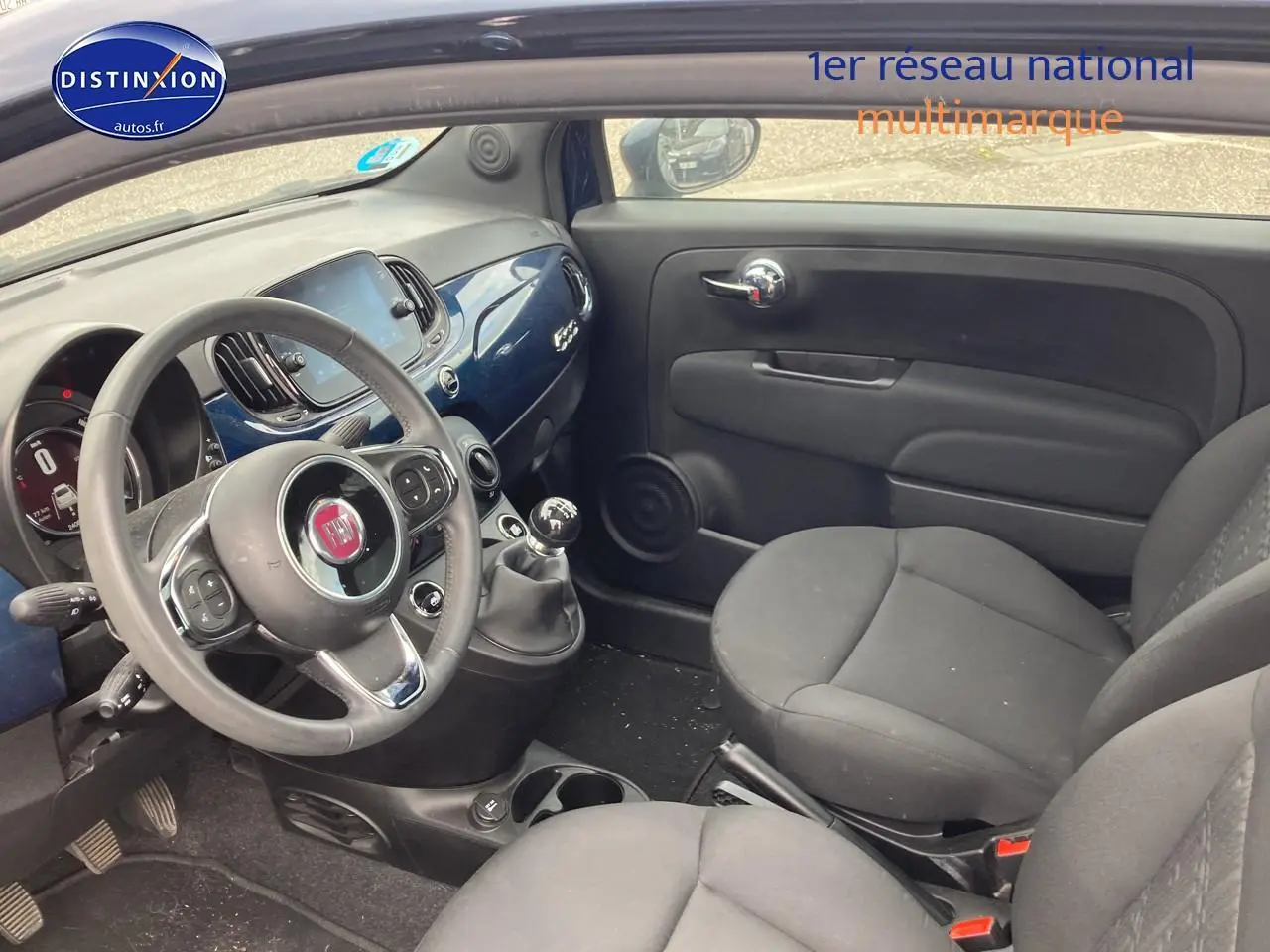 Vue intérieure côté conducteur de la Fiat 500 2023 avec tableau de bord bleu et volant cuir multifonction.