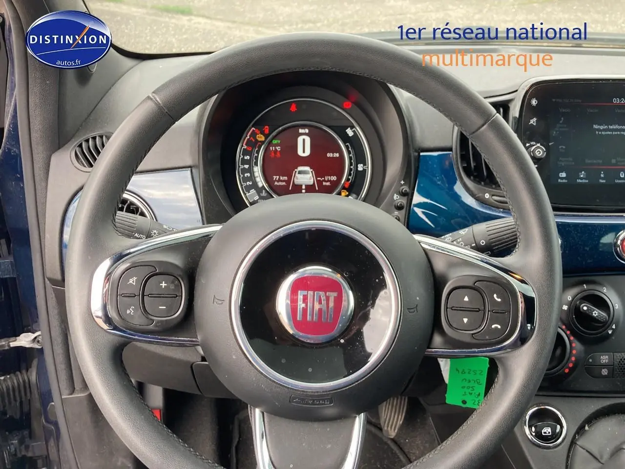Vue intérieure centrée sur le volant cuir multifonction noir de la Fiat 500 bleu, avec tableau de bord digital en arrière-plan.
