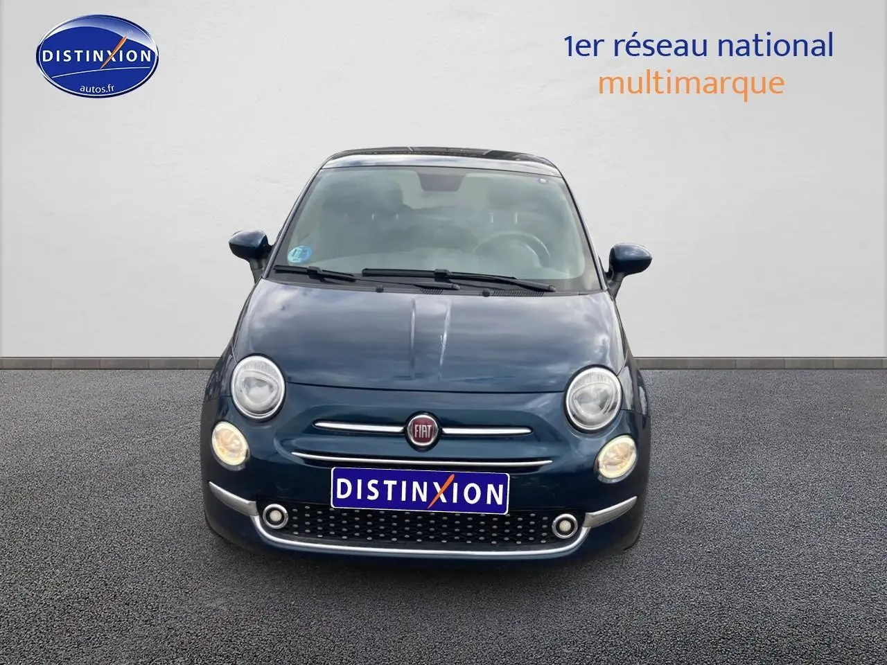 Vue frontale d'une FIAT 500 bleu foncé avec phares allumés et toit panoramique en verre visible.