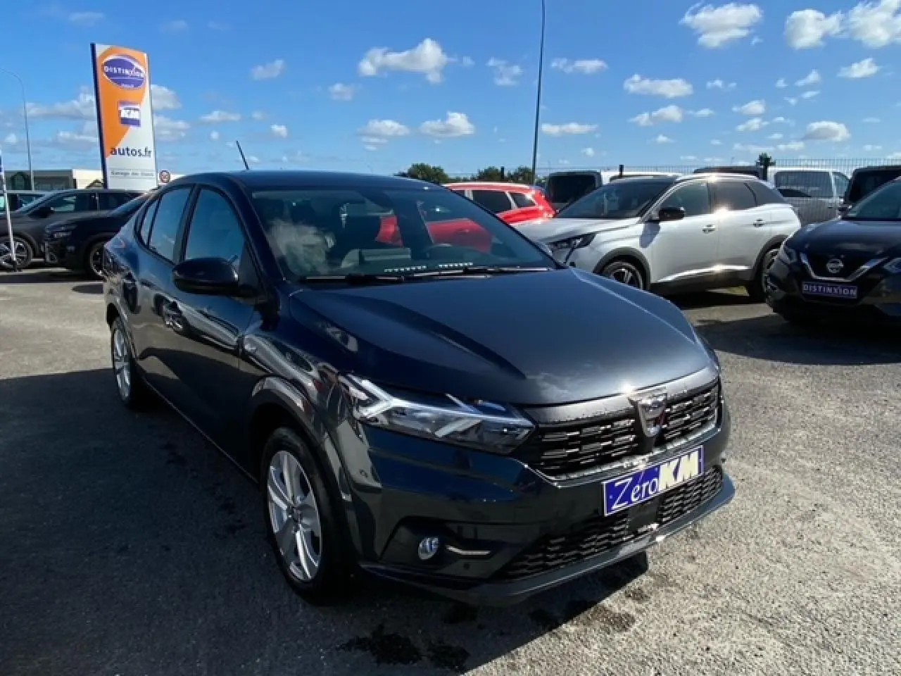 Dacia Logan gris vue 3/4 avant droit sur parking, avec calandre noire et phares LED allumés.