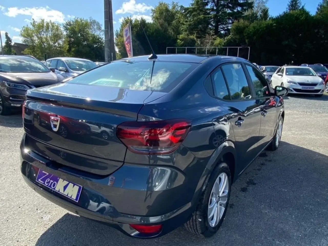 Vue 3/4 arrière droite d'une Dacia Logan gris métallisé 2022 avec feux arrière rouges et antenne de toit.