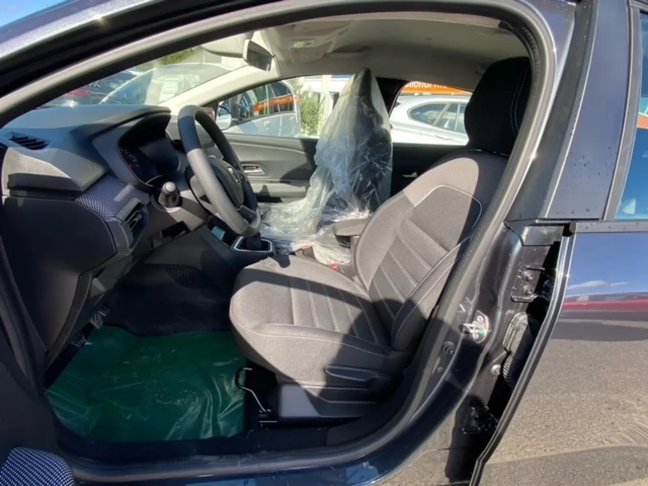 Vue intérieure côté conducteur de la Dacia Logan gris 2022, montrant les sièges et le volant avec plastique de protection.