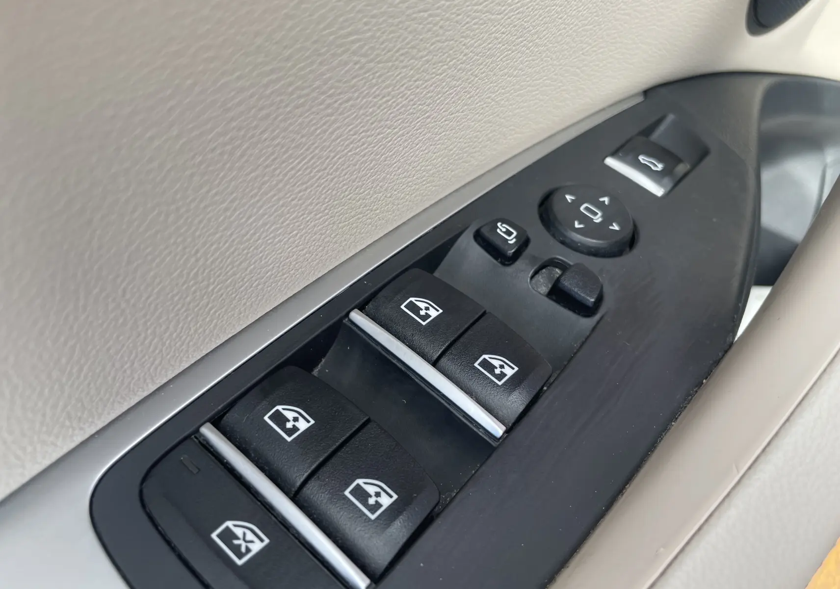 Gros plan sur les commandes de lève-vitres et réglages des rétroviseurs côté conducteur, intérieur beige du BMW X3 noir.