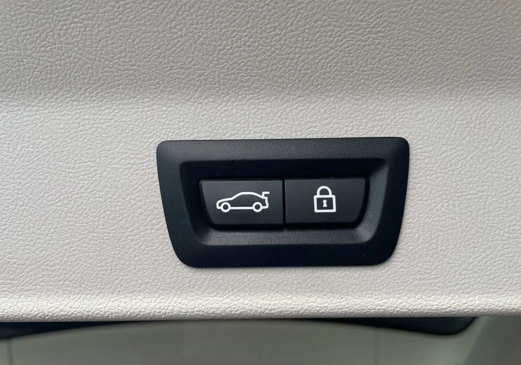 Boutons noirs de commande d'ouverture du coffre et de verrouillage, intégrés dans un panneau intérieur beige clair du BMW X3 noir (G01).
