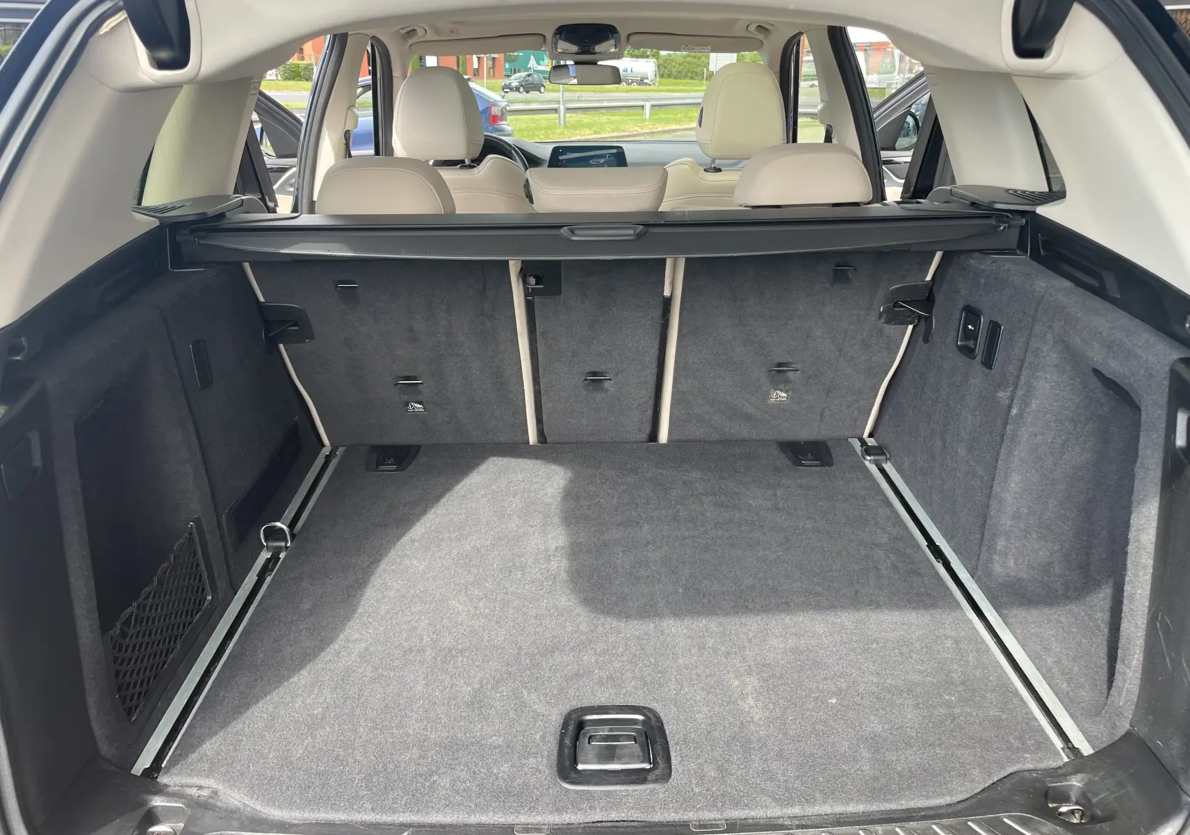 Coffre spacieux vu de l'arrière ouvert d'un BMW X3 noir 2021, avec banquette arrière beige et cache-bagages déployé.