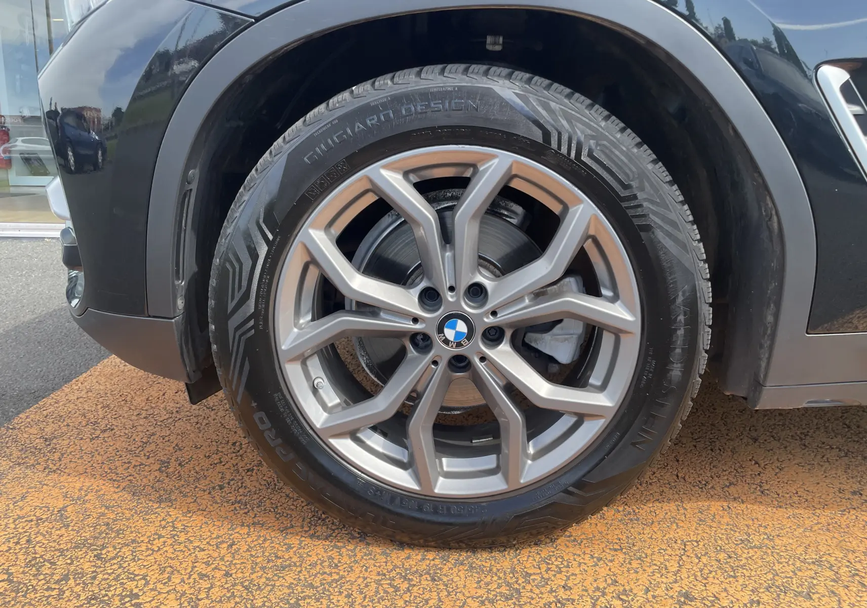 Gros plan sur la roue avant gauche noire d’un BMW X3 (G01) avec jante alliage à design moderne.