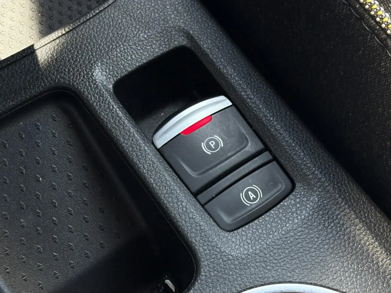 Gros plan sur les commandes du frein de parking électrique et de l’auto-hold dans la console centrale d’une Renault Symbioz noire.