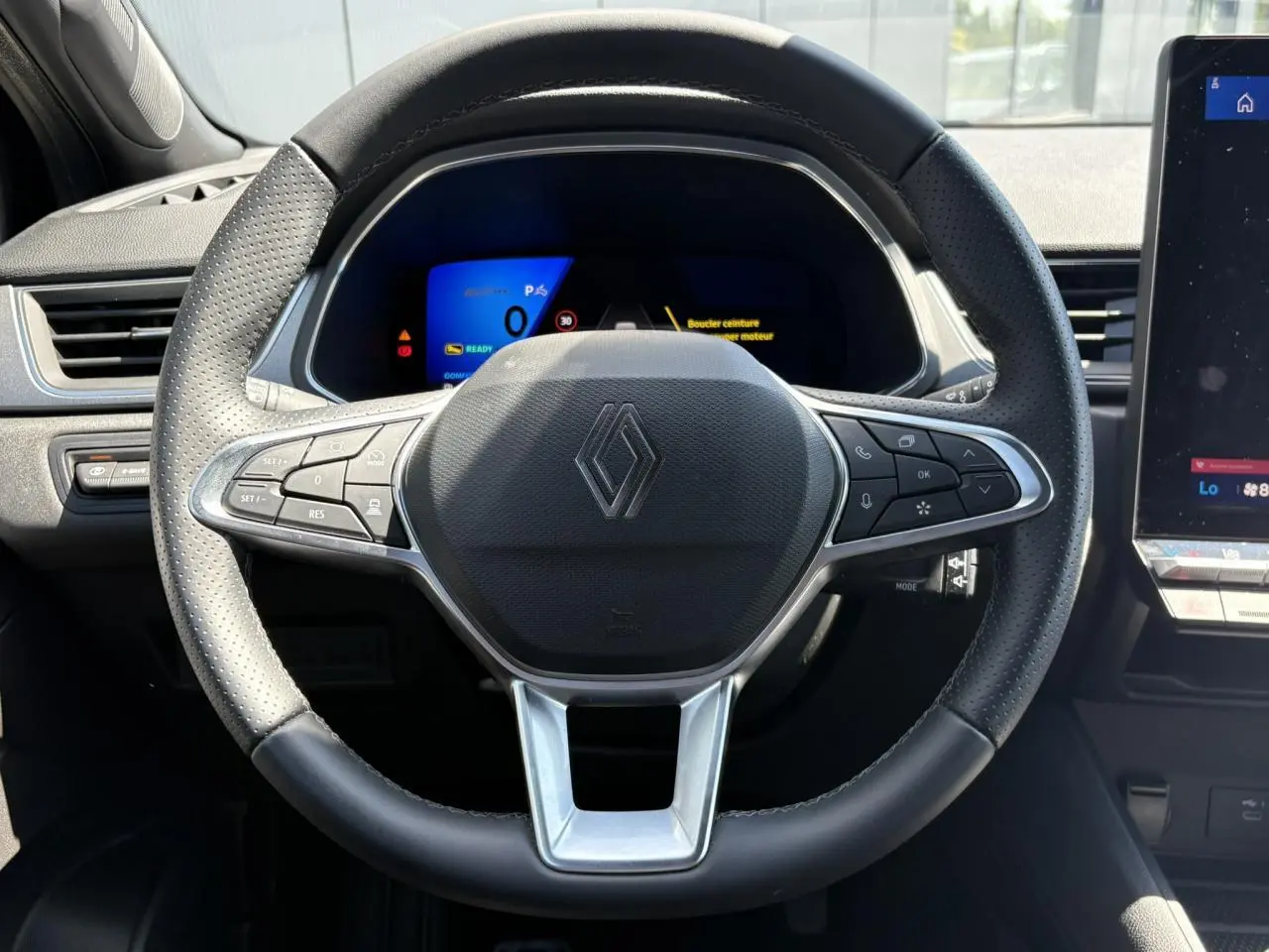 Vue frontale du volant noir perforé de la Renault SYMBIOZ 2025 avec tableau de bord numérique et écran tactile latéral.