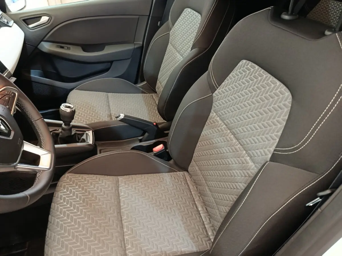 Vue intérieure côté conducteur de la Renault Clio Evolution TCe 90 2023, sièges tissu gris et volant cuir synthétique.
