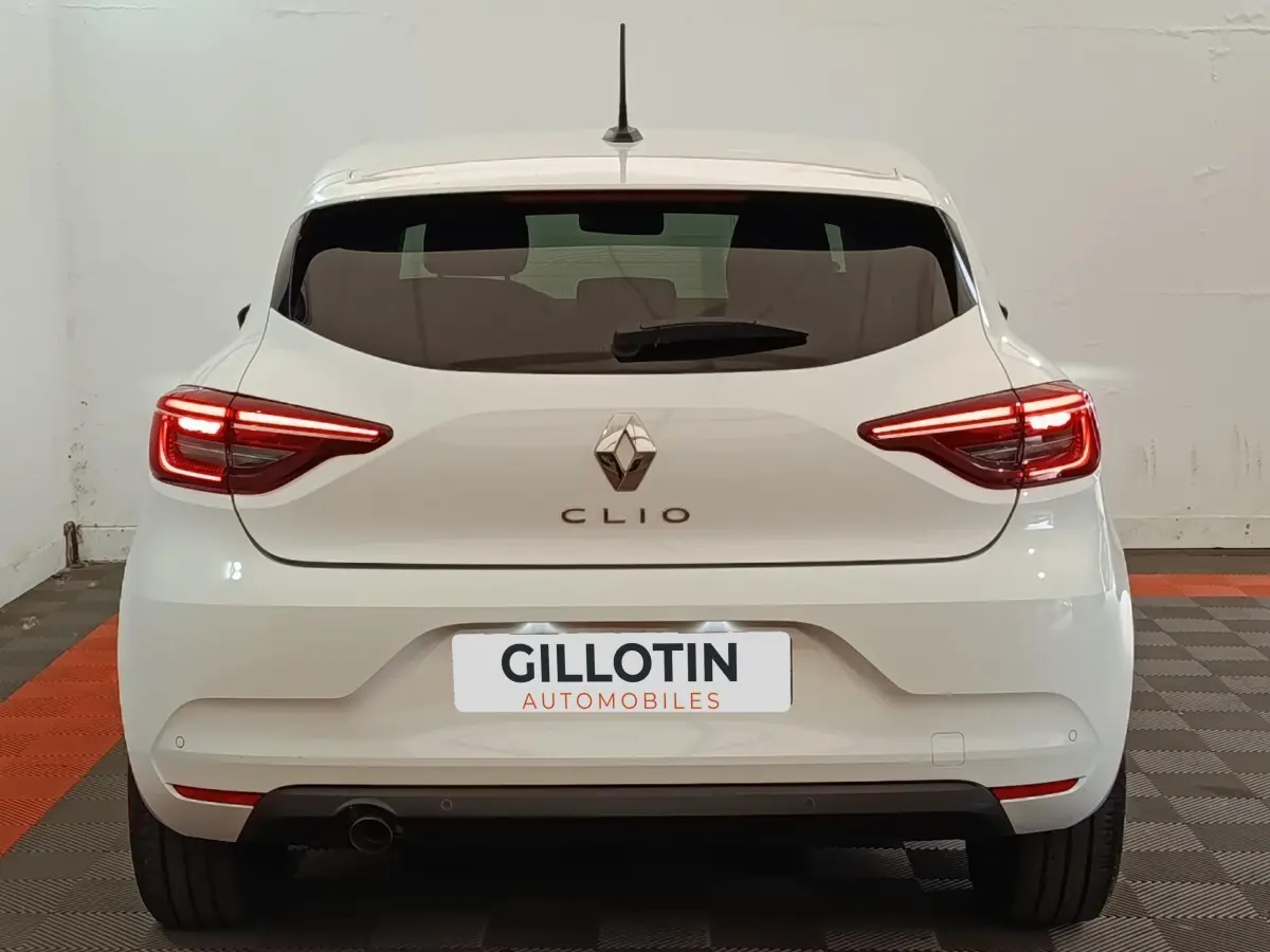 Vue arrière d'une Renault Clio blanche 2023 avec feux LED allumés et logo Renault bien visible.