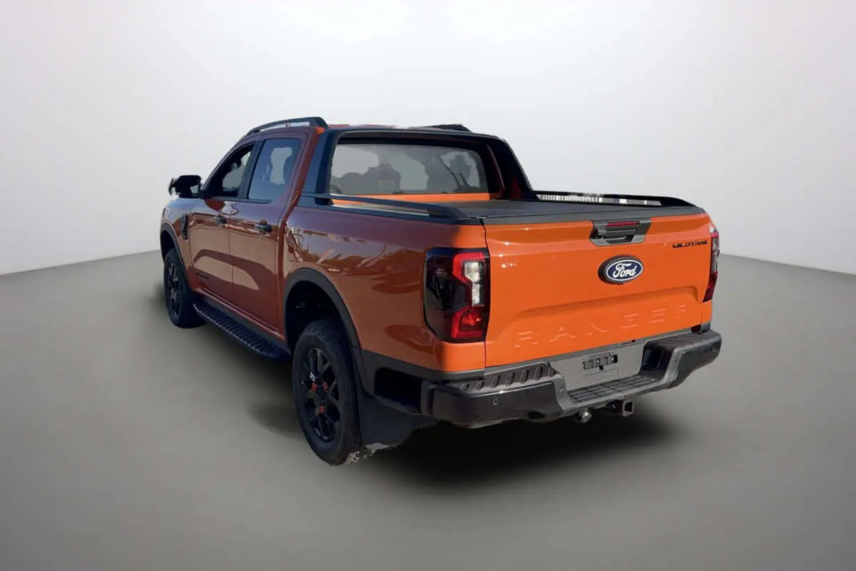 Ford Ranger Wildtrak orange Ignite vu en 3/4 arrière droit, avec benne et jantes noires tout-terrain.