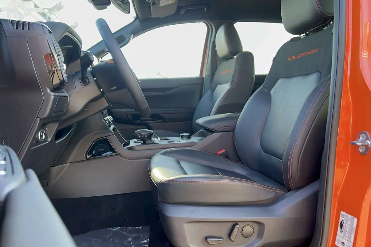 Vue intérieure côté conducteur du Ford Ranger Wildtrak 2026 orange Ignite avec sièges cuir noirs et surpiqûres orange.