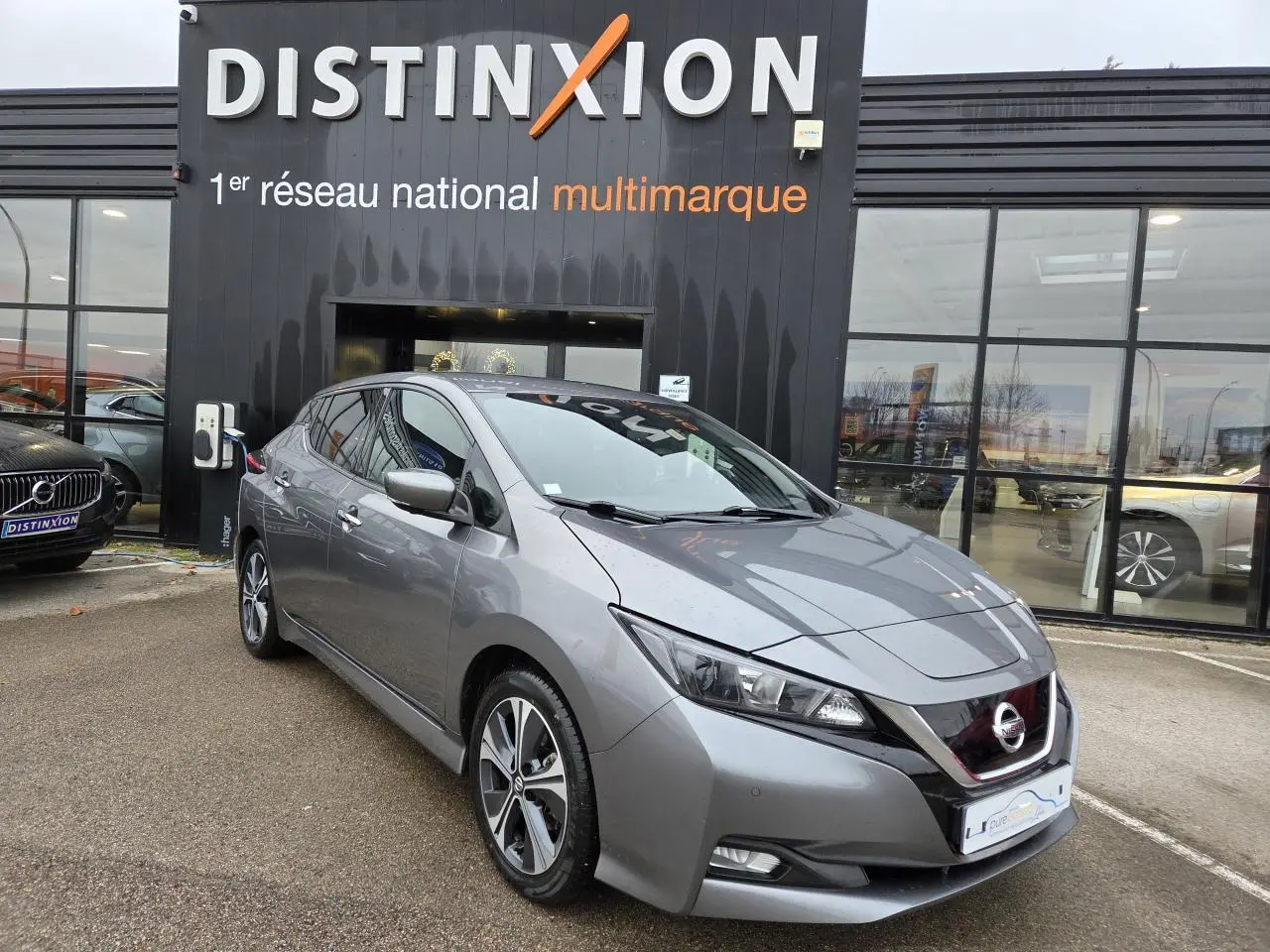 Nissan Leaf II gris foncé métallisé vue 3/4 avant droit devant un showroom Distinxion.