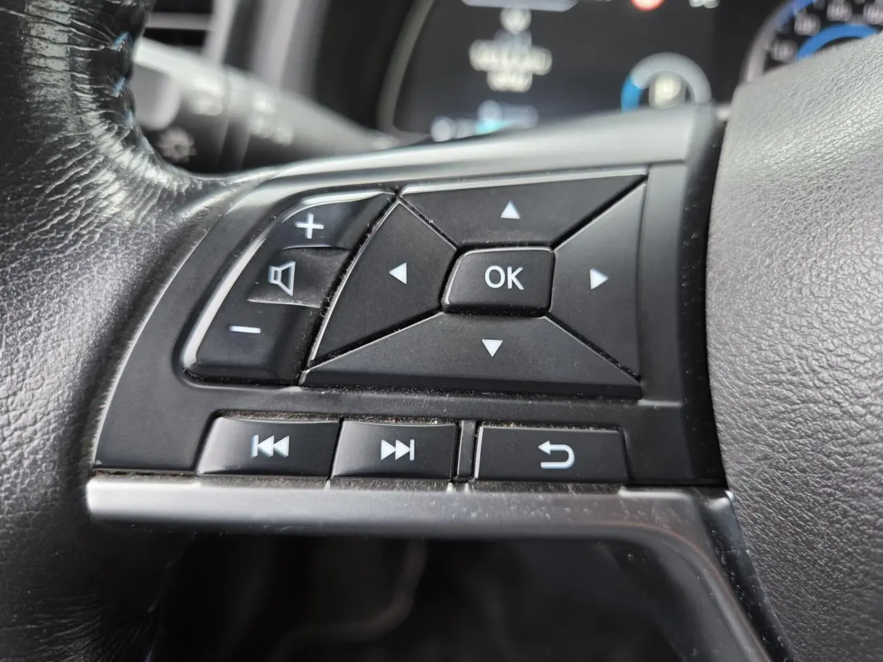 Gros plan sur les commandes multifonctions noires du volant cuir côté gauche du Nissan Leaf II gris foncé 2021.
