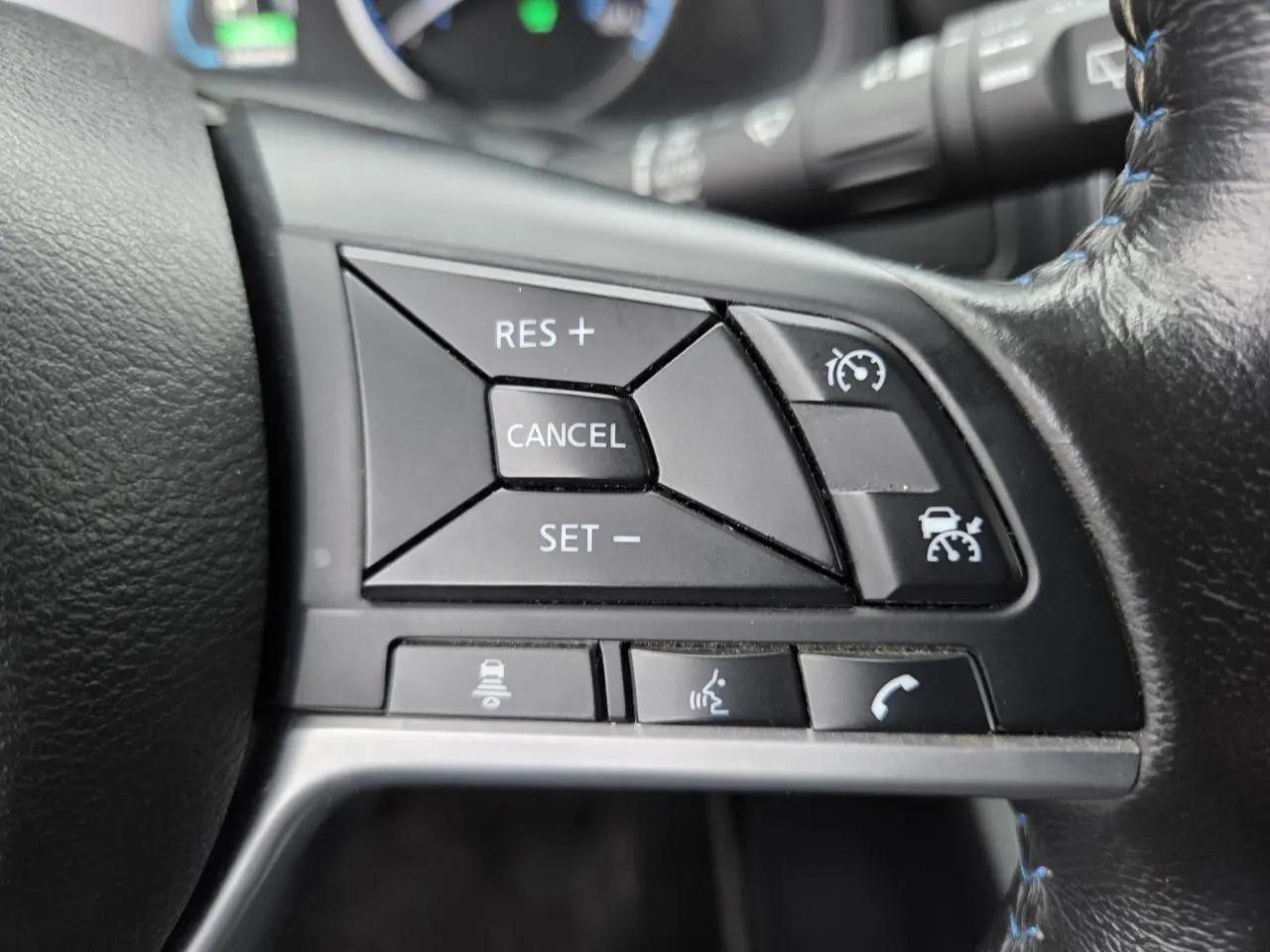 Gros plan sur les commandes du régulateur de vitesse au volant cuir noir d'une Nissan Leaf II gris foncé 2021.