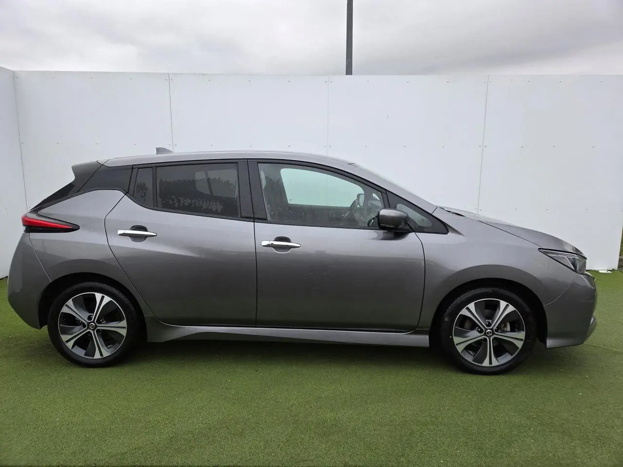 Vue de profil côté gauche d'une Nissan Leaf II gris foncé métallisé avec jantes alliage et vitres teintées.