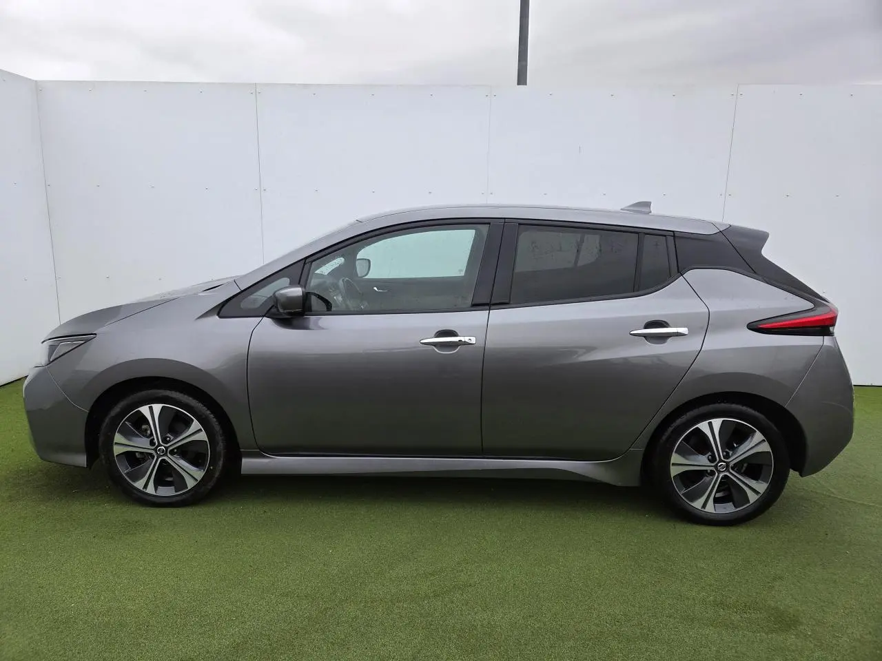 Vue de profil côté gauche d'une Nissan Leaf II gris foncé métallisé avec jantes alliage et vitres teintées.