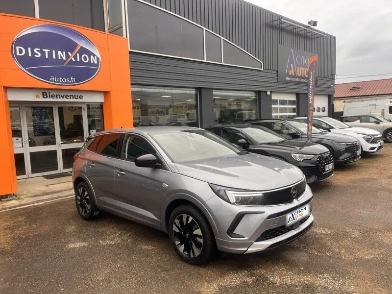 Vue 3/4 avant droite d'un Opel Grandland gris Kontrast métallisé avec jantes bi-ton, stationné devant un garage.