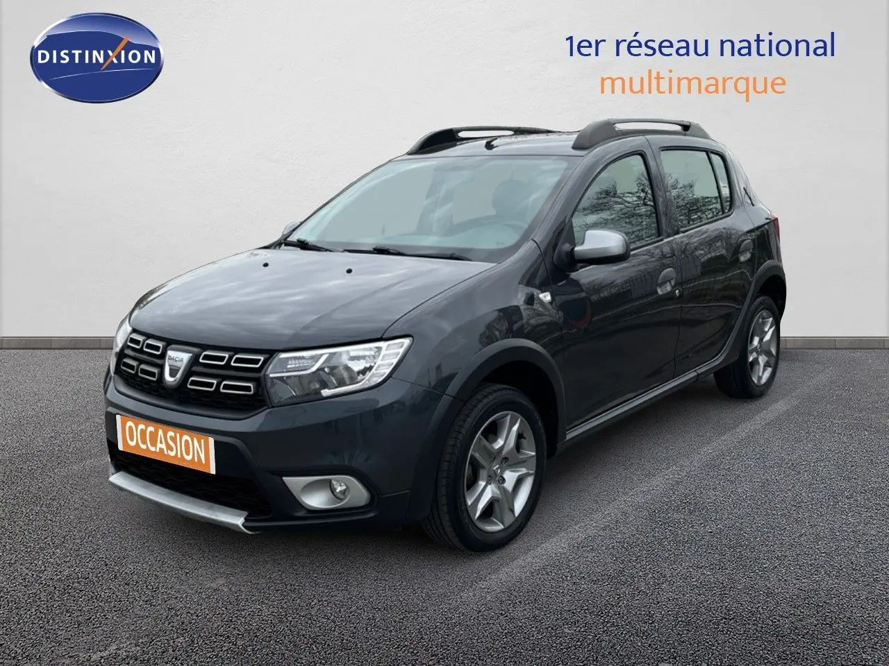 Dacia Sandero Stepway gris foncé vue 3/4 avant droit avec barres de toit et jantes alliage.