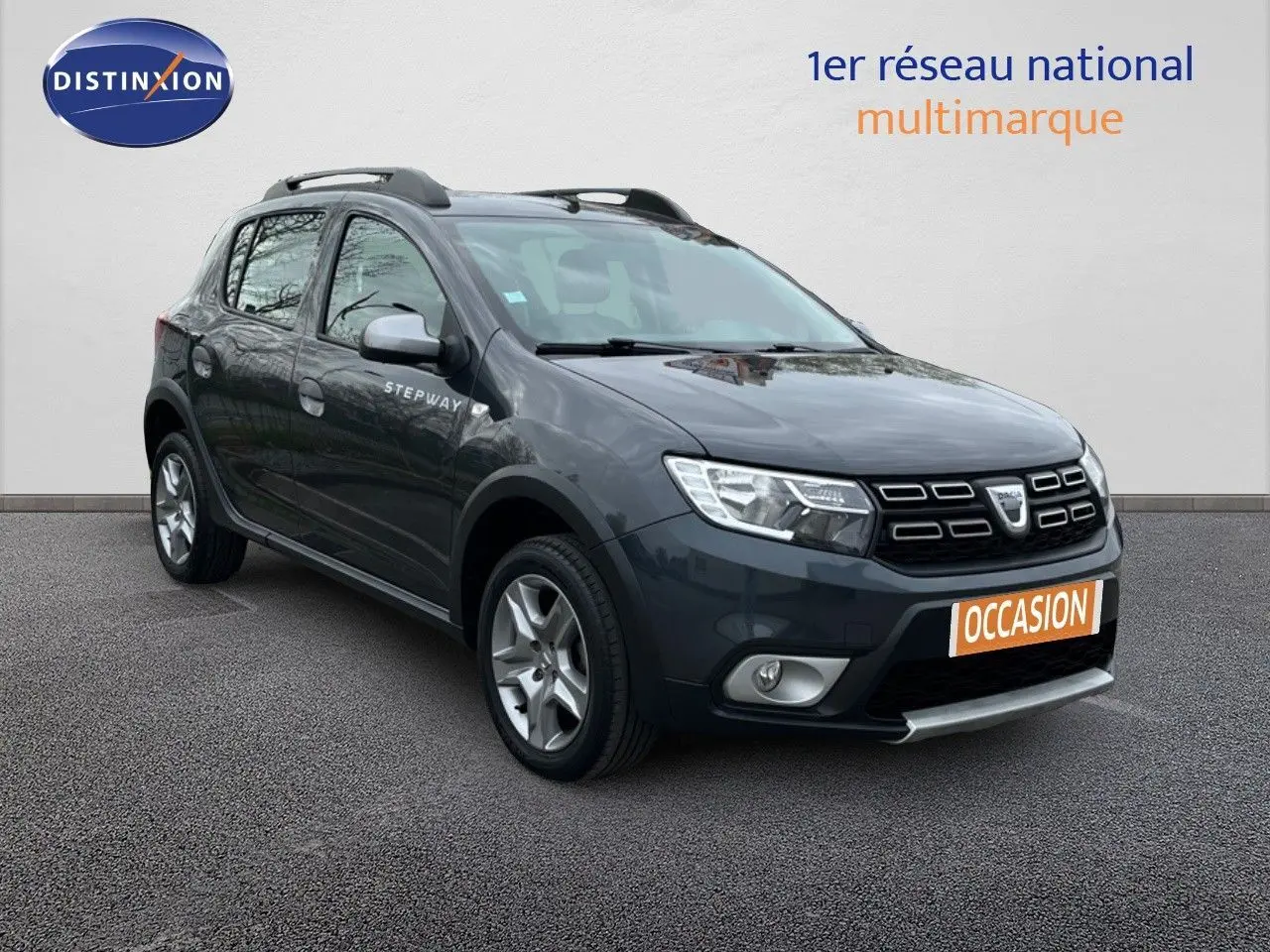 Vue 3/4 avant d'une Dacia Sandero Stepway 0.9 TCe gris foncé avec barres de toit et jantes alliage.