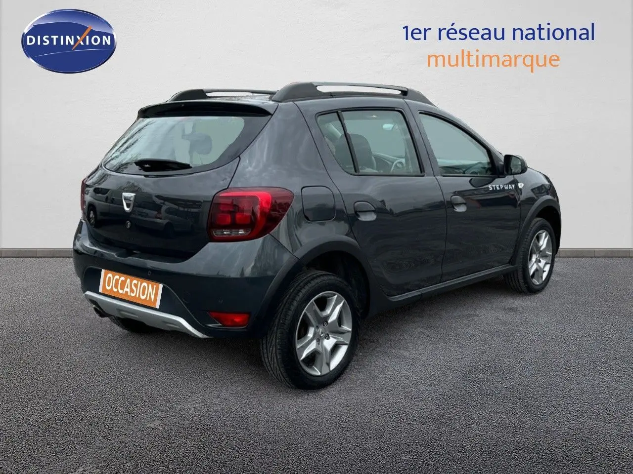 Vue 3/4 arrière droite d'une Dacia Sandero Stepway 0.9 TCe gris foncé de 2016 avec badge Stepway sur la porte.