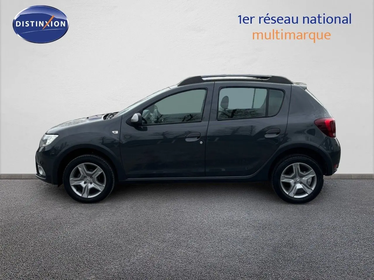 Profil côté gauche d'une Dacia Sandero Stepway 0.9 TCe gris foncé essence de 2016, avec barres de toit visibles.